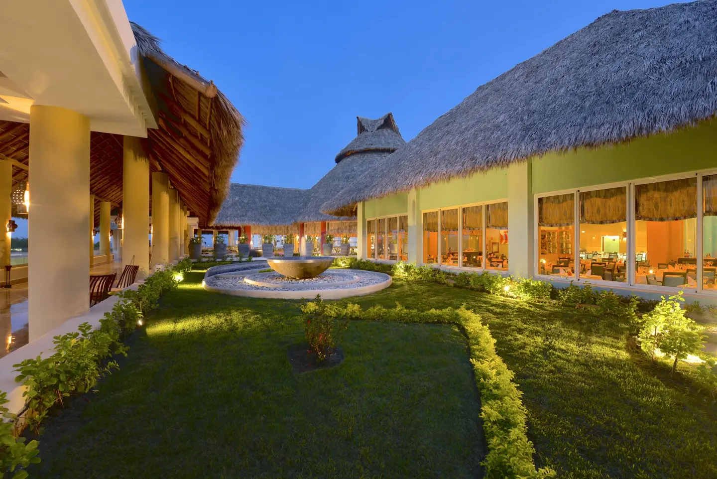 Thatched-roof resort buildings frame a lit garden courtyard at Iberostar Selection Playa Mita.