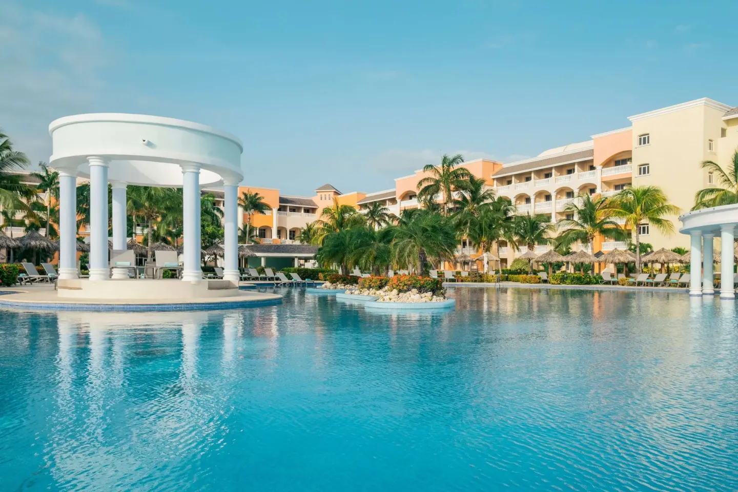 Large pool with white pavilions and palm landscaping at Iberostar Selection Rose Hall Suites.