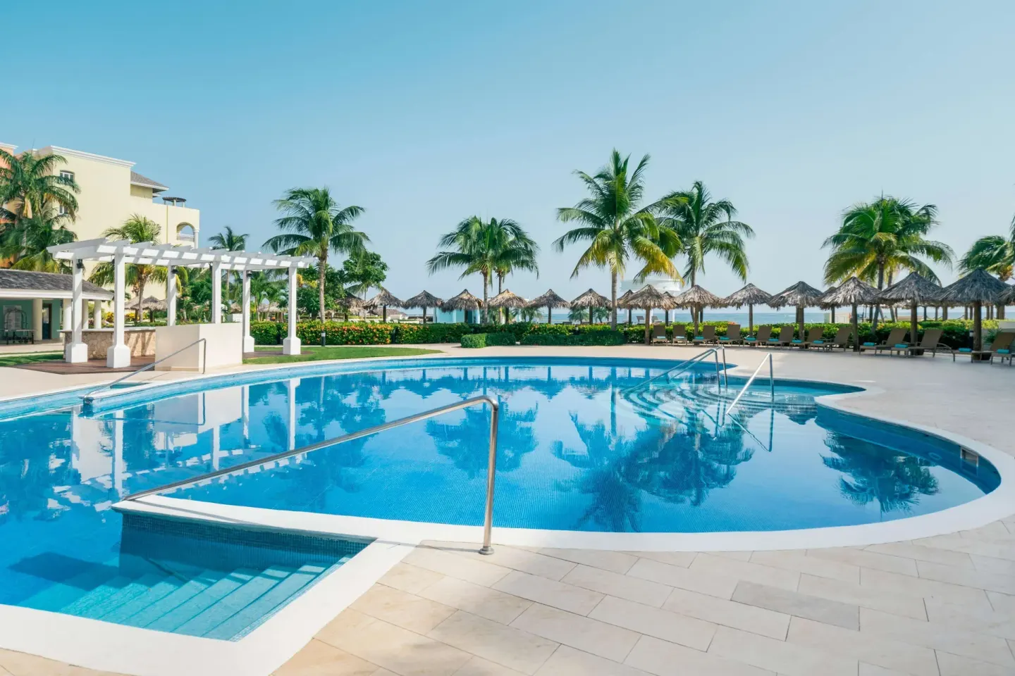 Quiet pool with palm trees and thatched shade huts at Iberostar Selection Rose Hall Suites.