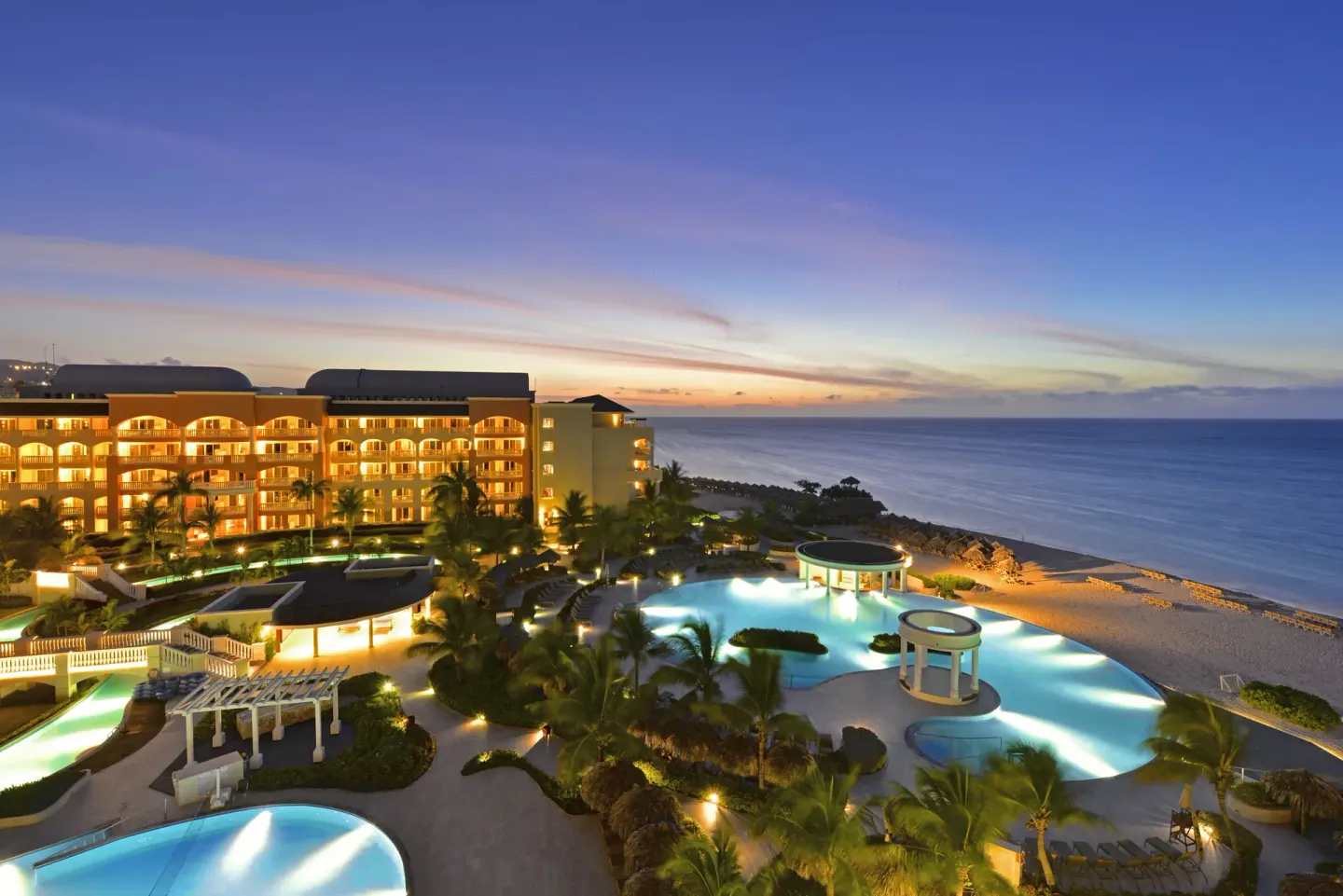 Resort pools, beach, and ocean at dusk at Iberostar Selection Rose Hall Suites.