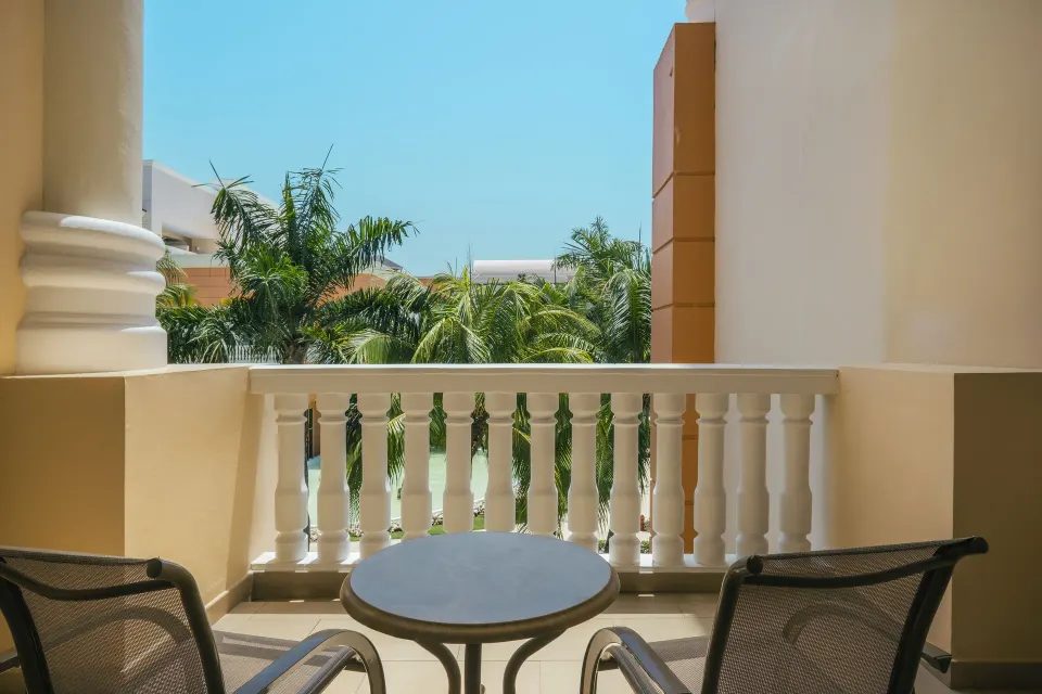 Junior Suite balcony with chairs, a round table, and palms at Iberostar Selection Rose Hall Suites.