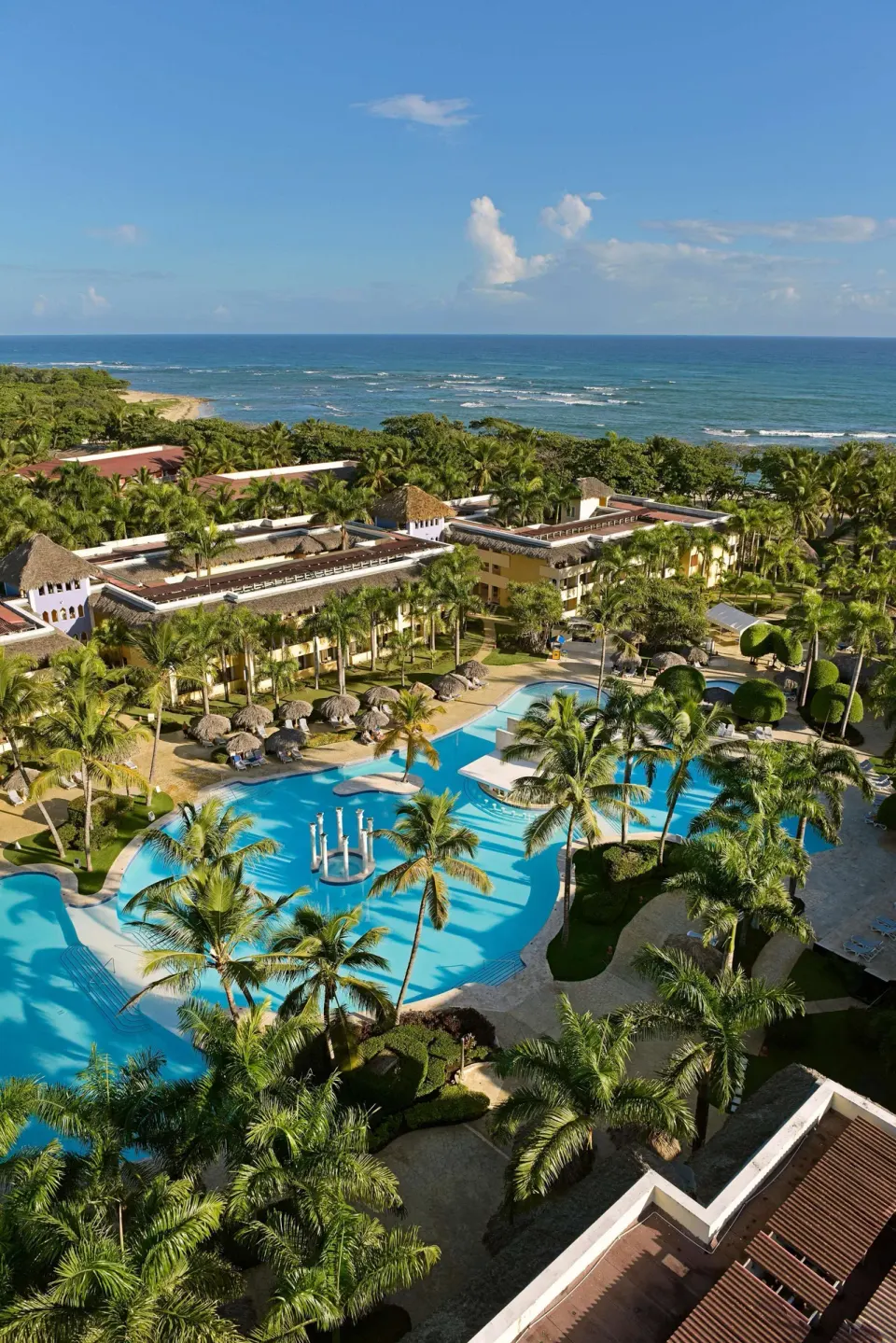 Aerial view of pools, palms, resort buildings, and ocean at Iberostar Waves Costa Dorada.
