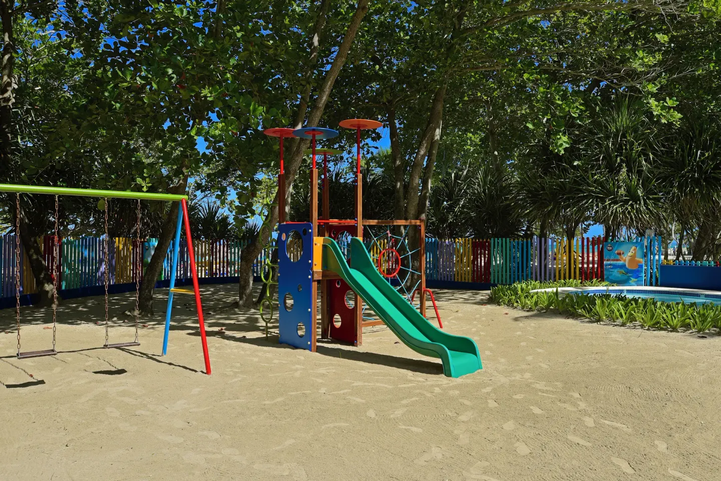 Shaded children's playground with swings and a slide at Iberostar Waves Costa Dorada.