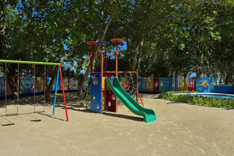 Shaded children's playground with swings and a slide at Iberostar Waves Costa Dorada.