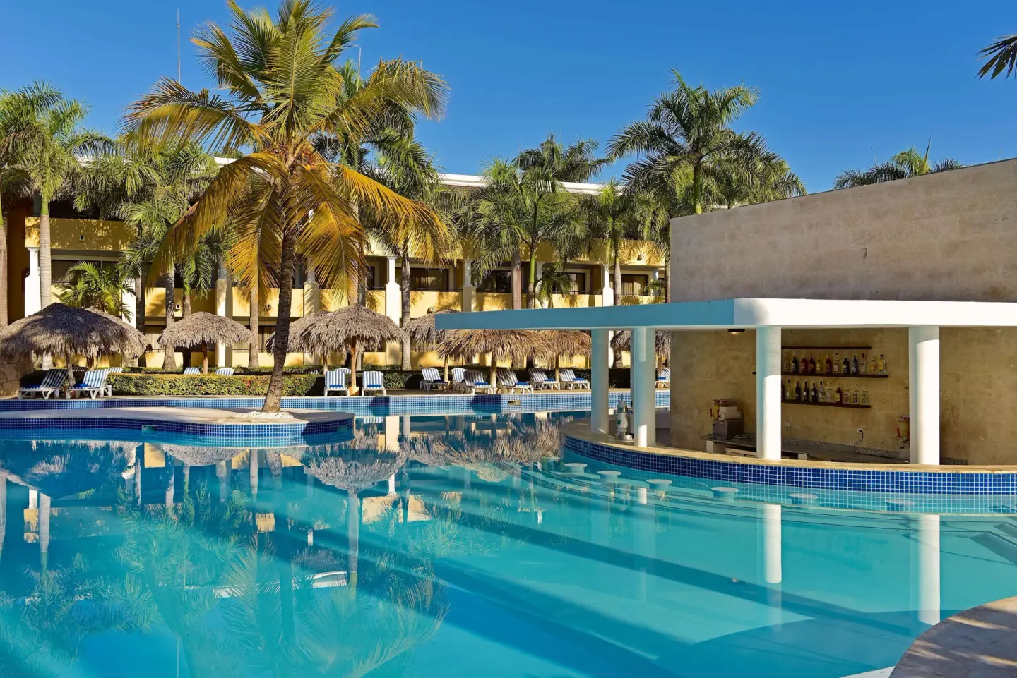 Curved resort pool and swim-up bar with palms at Iberostar Waves Costa Dorada.