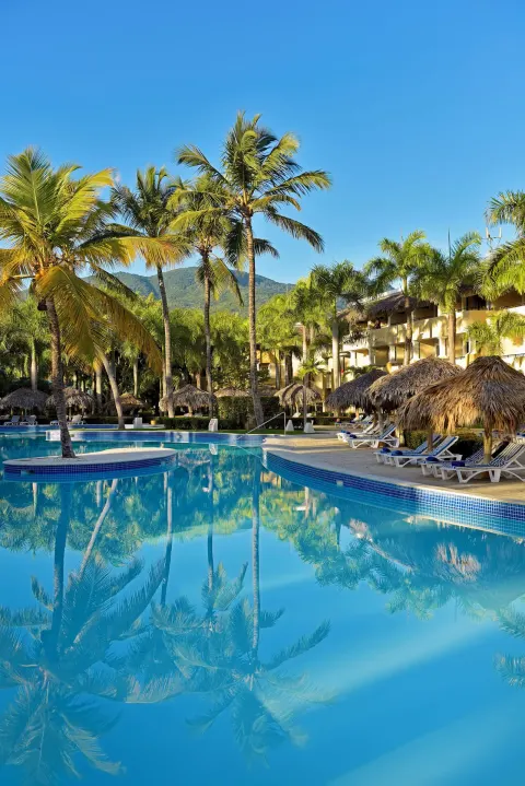 Curved pool bordered by palms and thatched umbrellas at Iberostar Waves Costa Dorada.