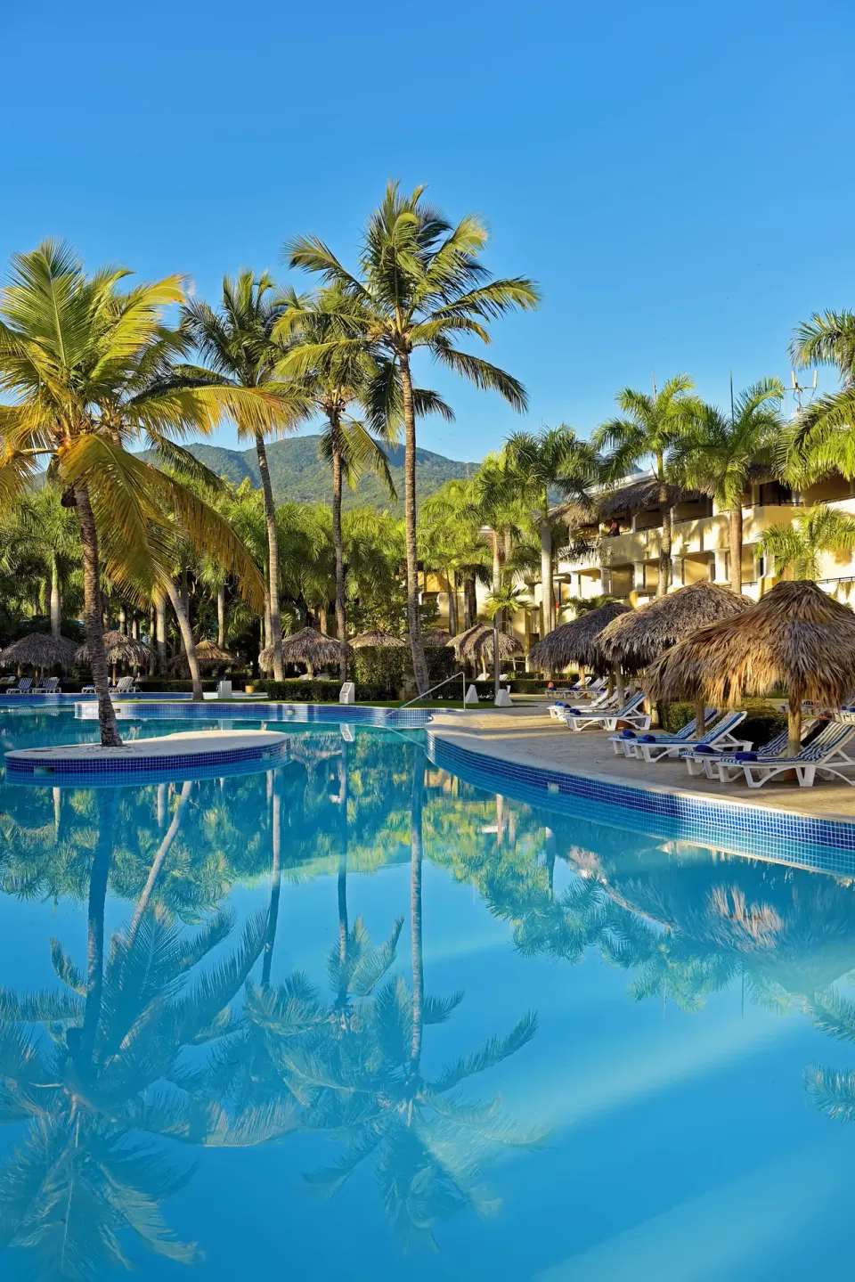 Curved pool bordered by palms and thatched umbrellas at Iberostar Waves Costa Dorada.