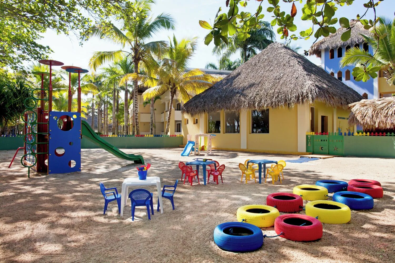Kids' play area with tables, painted tires, and a slide at Iberostar Waves Costa Dorada.