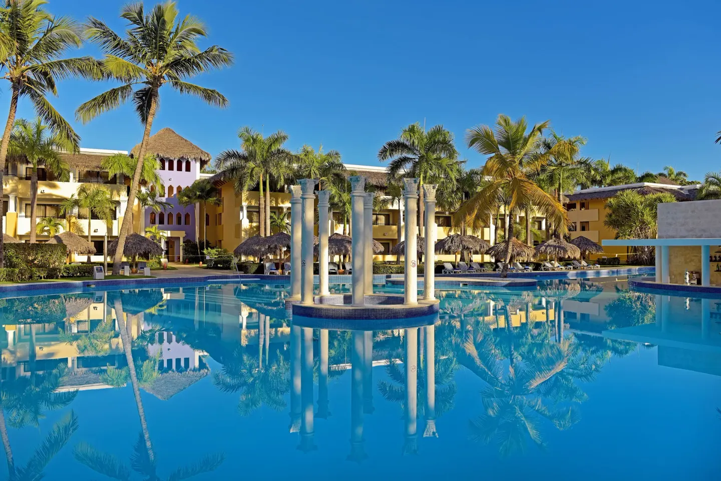 Main pool with decorative columns and palms at Iberostar Waves Costa Dorada.