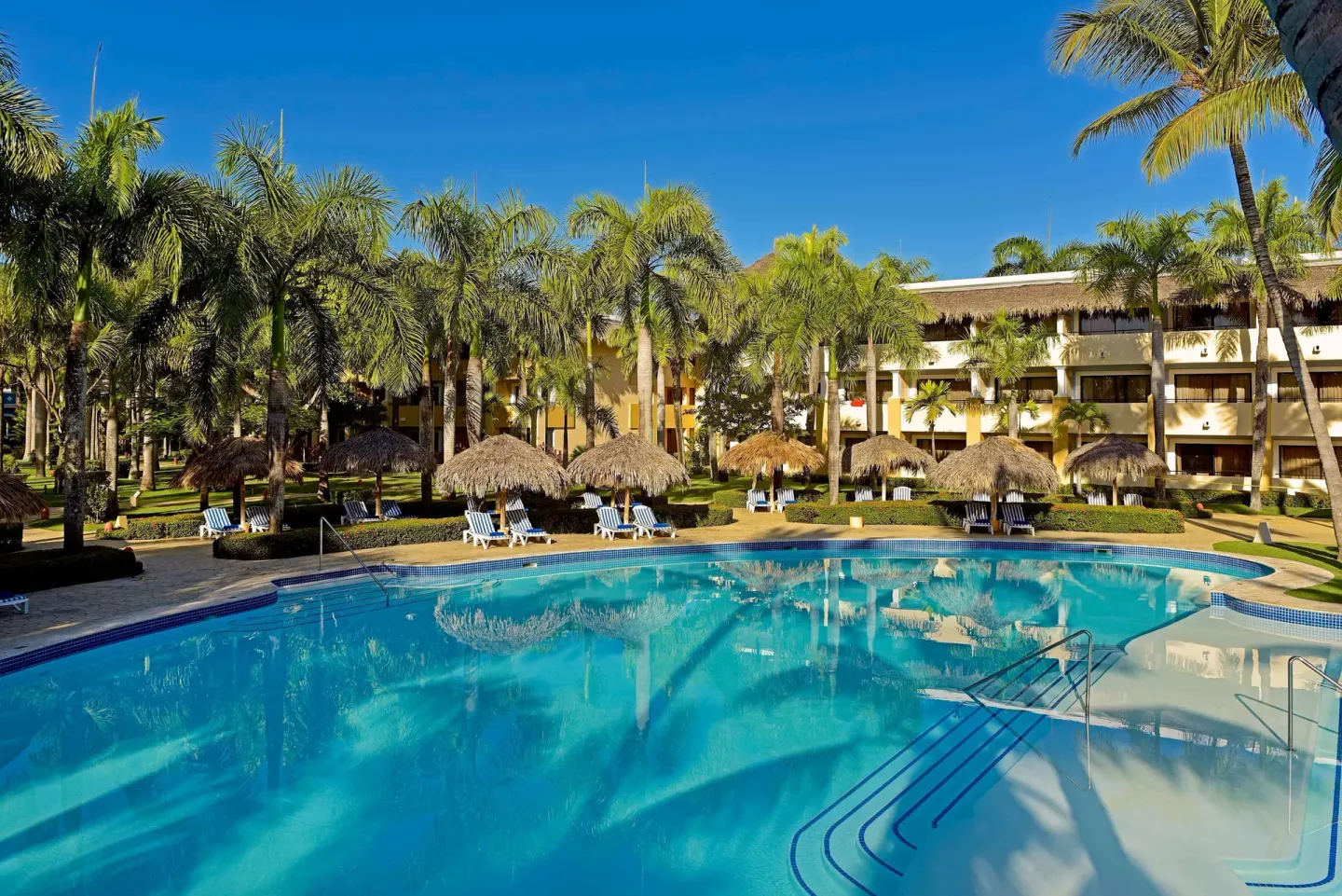 Main pool bordered by palapas, palms, and guest buildings at Iberostar Waves Costa Dorada.