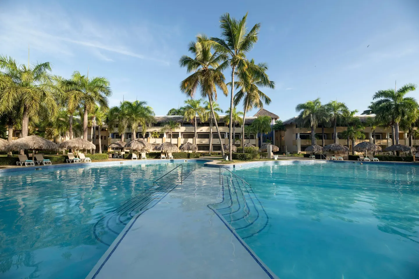 Wide pool with central walkway and palm trees at Iberostar Waves Costa Dorada.