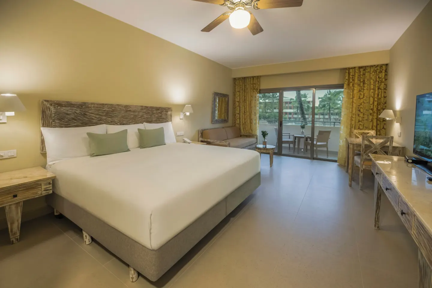 King guest room with balcony doors, sofa, TV and ceiling fan at Iberostar Waves Dominicana.