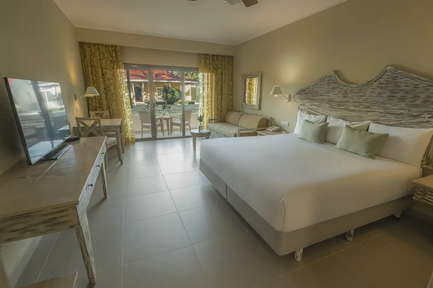 Guest room with king bed, sofa, TV and patio doors at Iberostar Waves Dominicana.