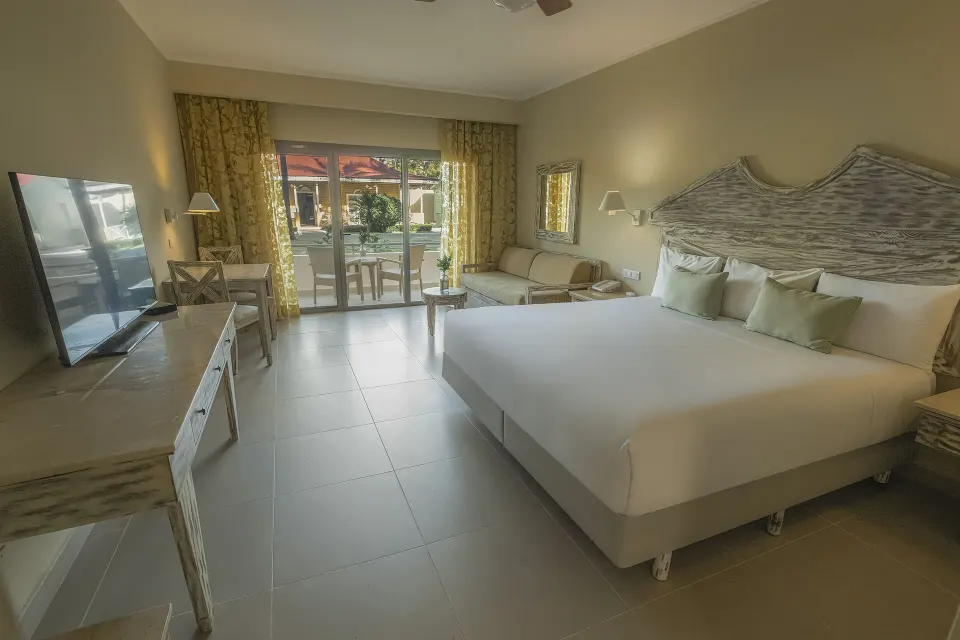 Guest room with king bed, sofa, TV and patio doors at Iberostar Waves Dominicana.