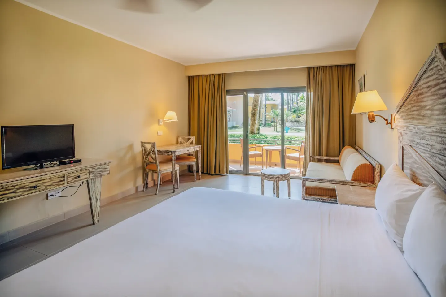 King guest room with patio doors, TV console, desk and sofa at Iberostar Waves Dominicana.