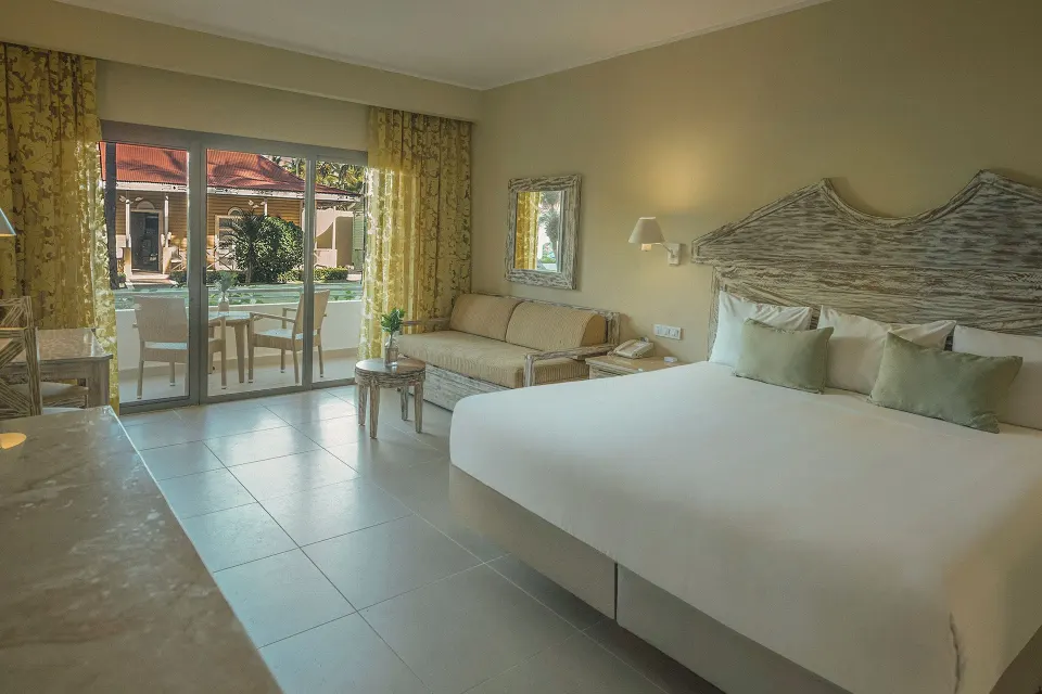 King guest room with sofa, balcony doors and rustic headboard at Iberostar Waves Dominicana.