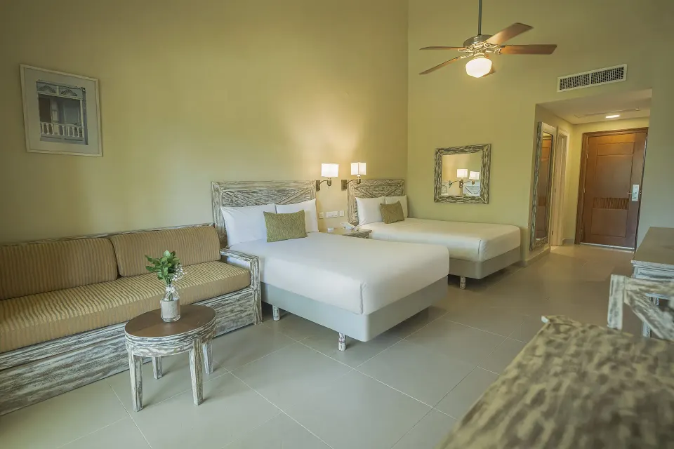 Guest room with two beds, striped sofa and ceiling fan at Iberostar Waves Dominicana.