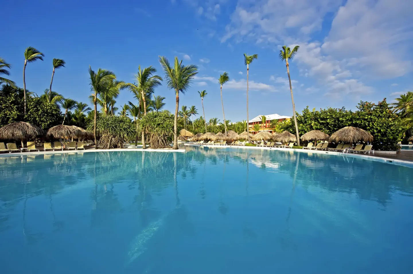 Blue resort pool with palms and thatched umbrellas at Iberostar Waves Dominicana.