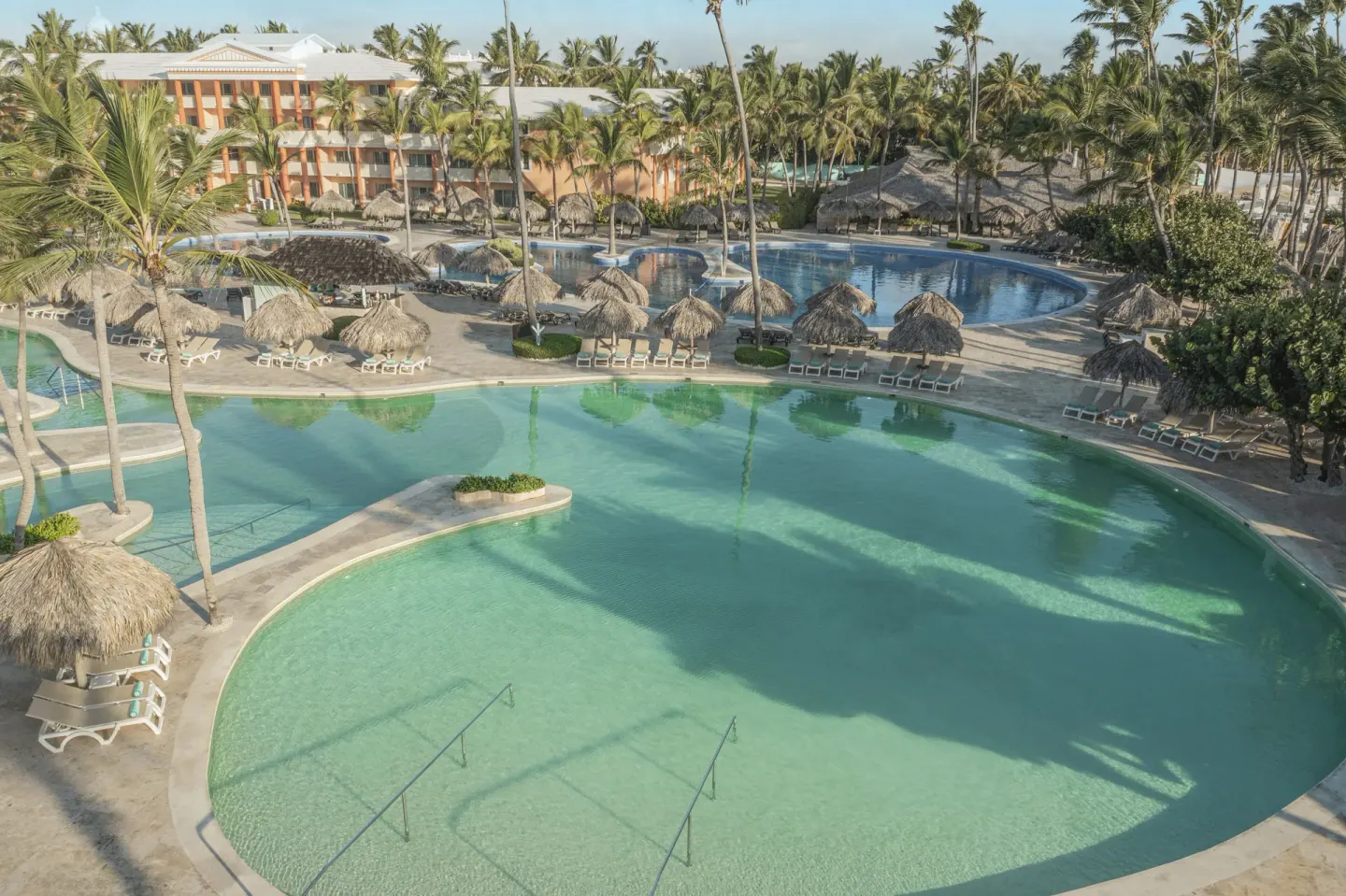 Large resort pools with palapas and palm trees at Iberostar Waves Dominicana.