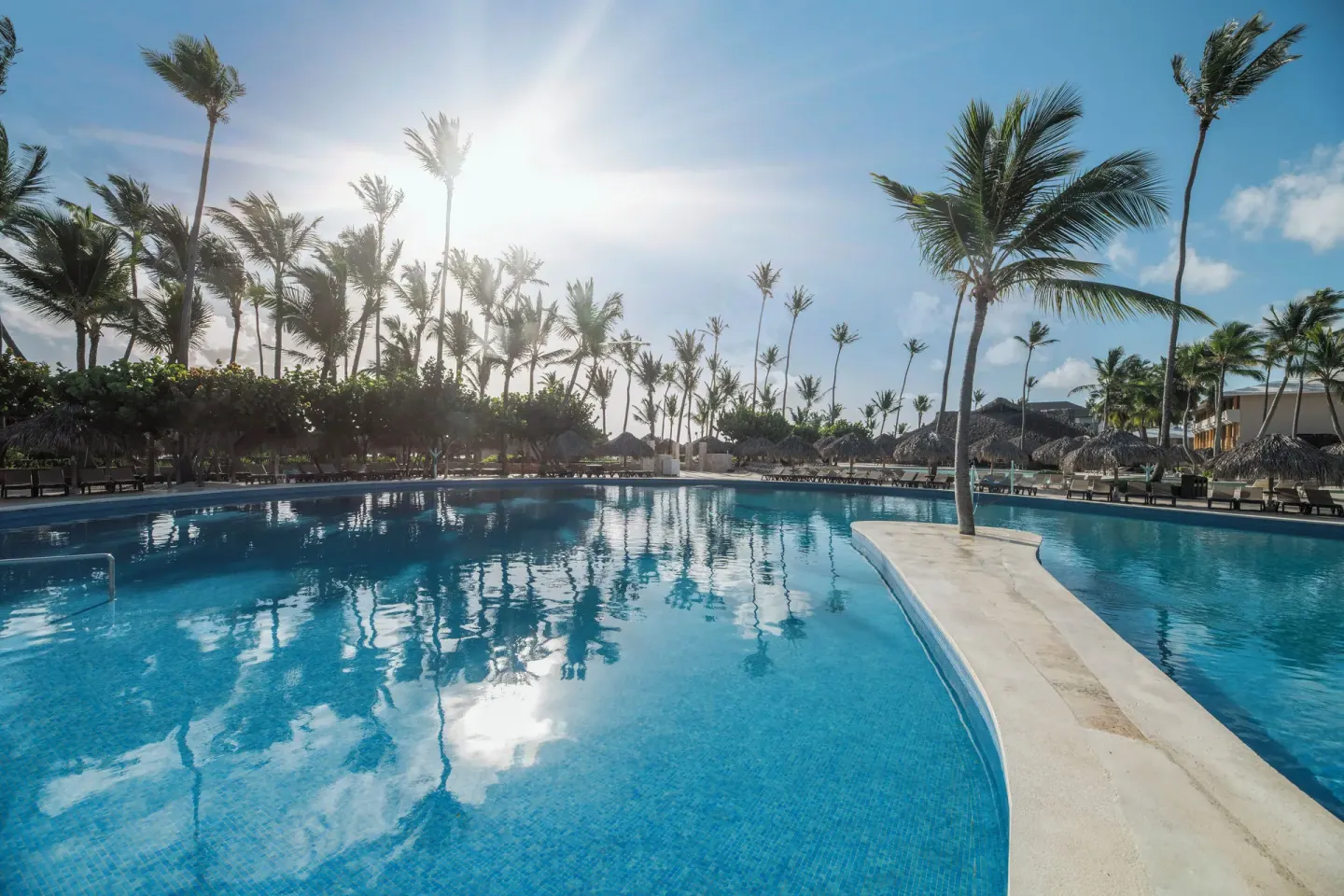 Sunlit pool with palm reflections and a narrow walkway at Iberostar Waves Dominicana.