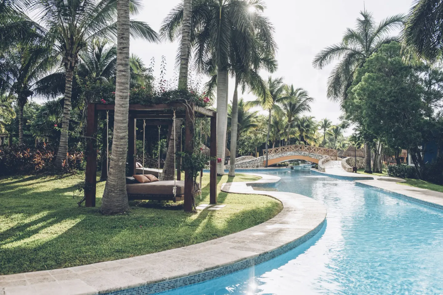 Lazy river pool beside palms and a bridge at Iberostar Waves Paraíso Beach.