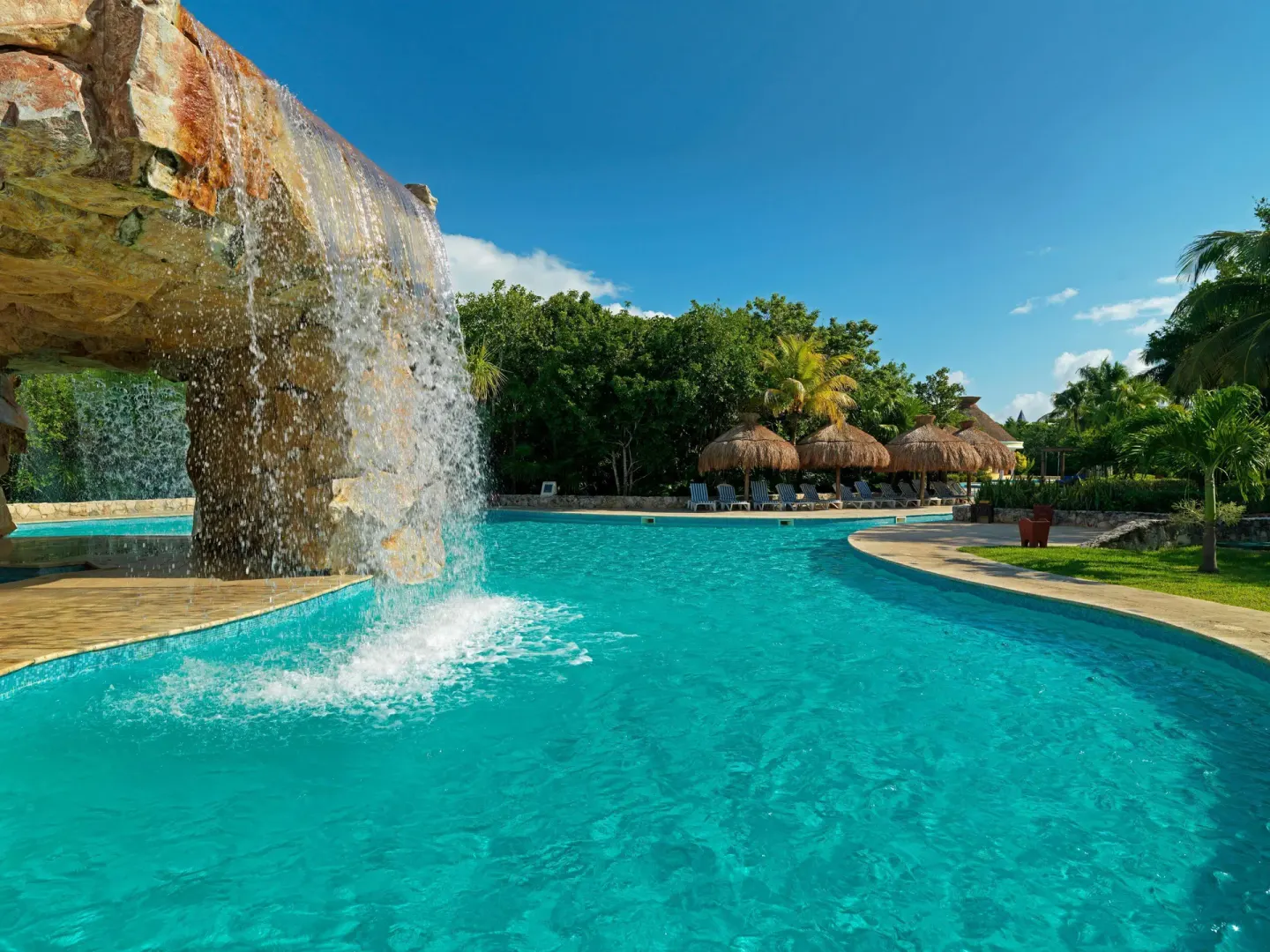 Rock waterfall flowing into a turquoise pool at Iberostar Waves Paraíso Beach.
