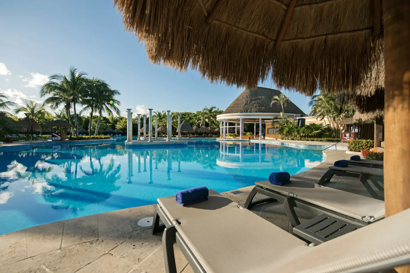 Poolside loungers under a thatched roof at Iberostar Waves Paraíso Beach.