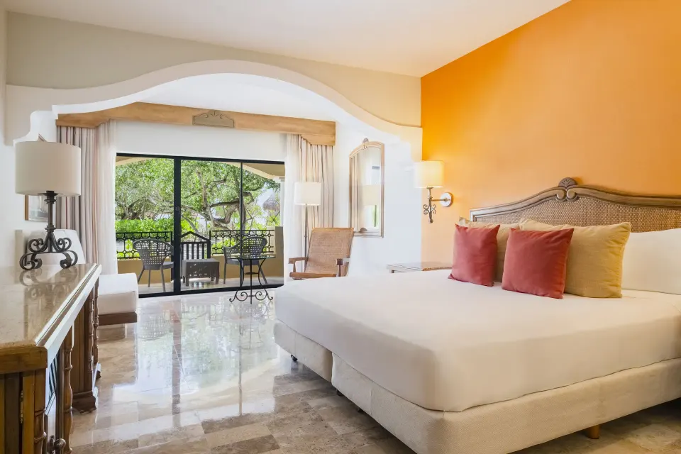 Junior Suite king bed at Iberostar Waves Paraíso Beach with a furnished terrace beyond sliding glass doors.
