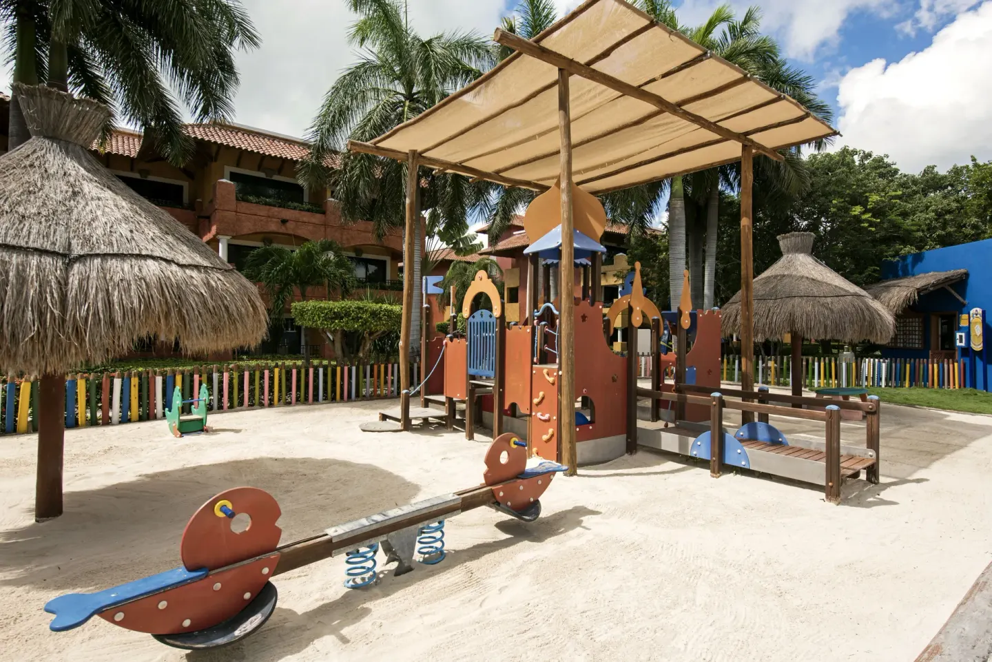 Outdoor children’s playground with sand, shade huts, and play structures at Iberostar Waves Paraíso del Mar.