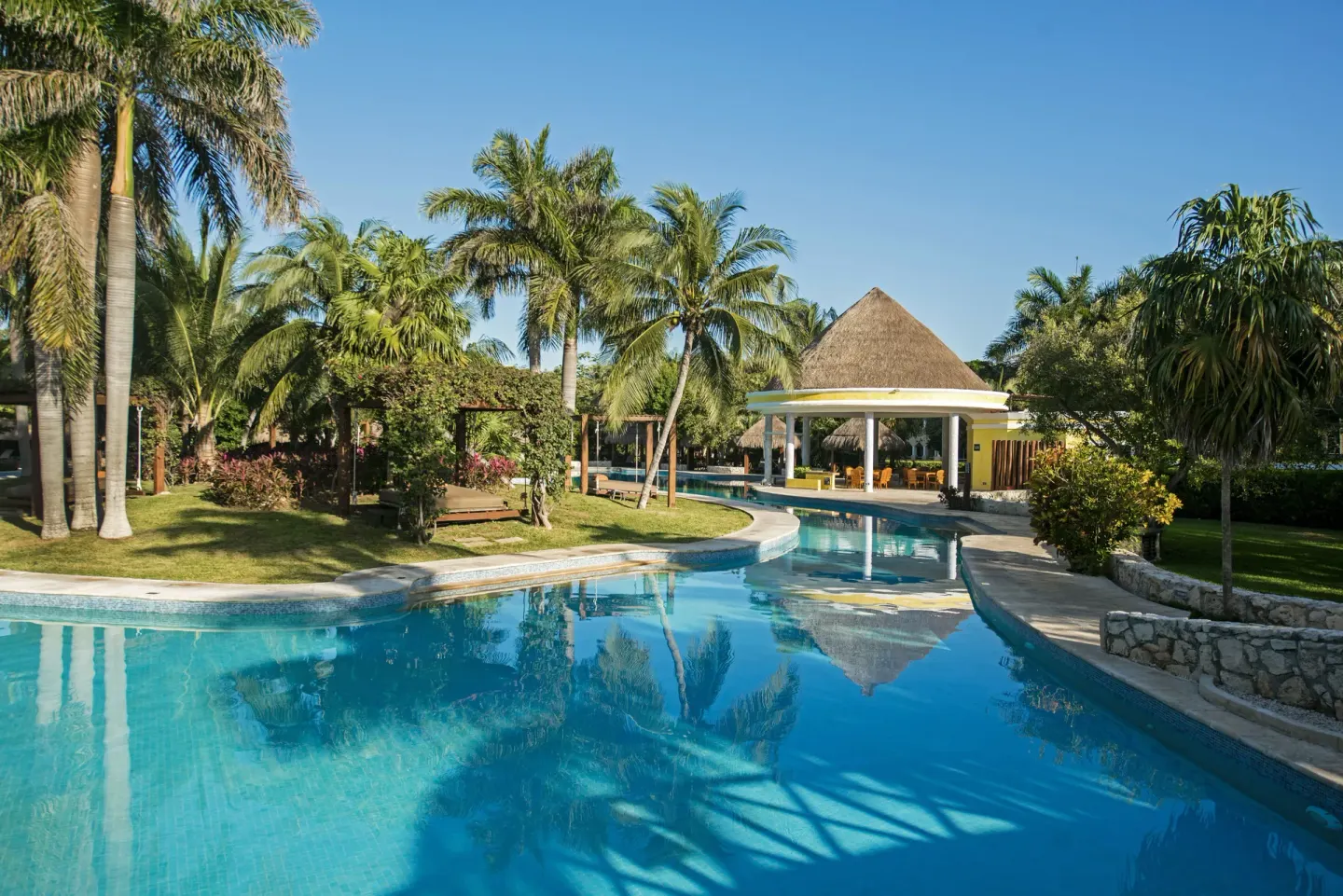 Pool channel with palms and a thatched pavilion at Iberostar Waves Paraíso del Mar.