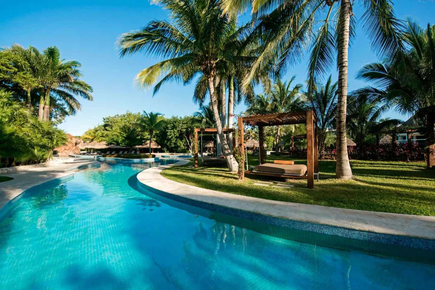 Poolside cabanas and palms beside a curved pool at Iberostar Waves Paraíso del Mar.
