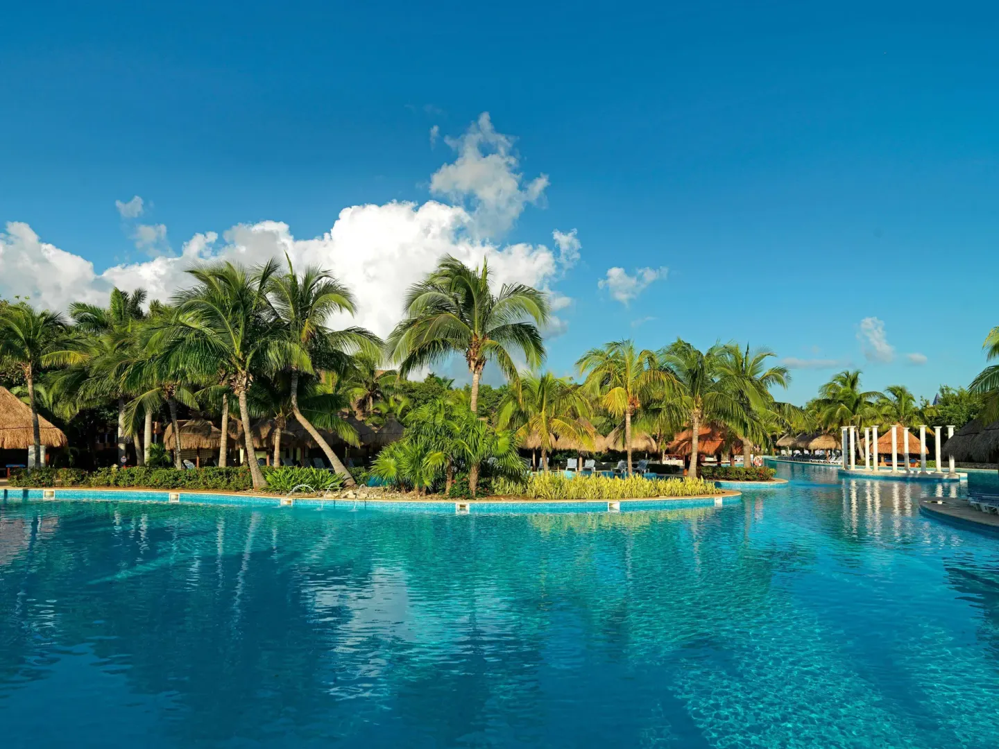 Wide pool view with palm islands and blue sky at Iberostar Waves Paraíso del Mar.