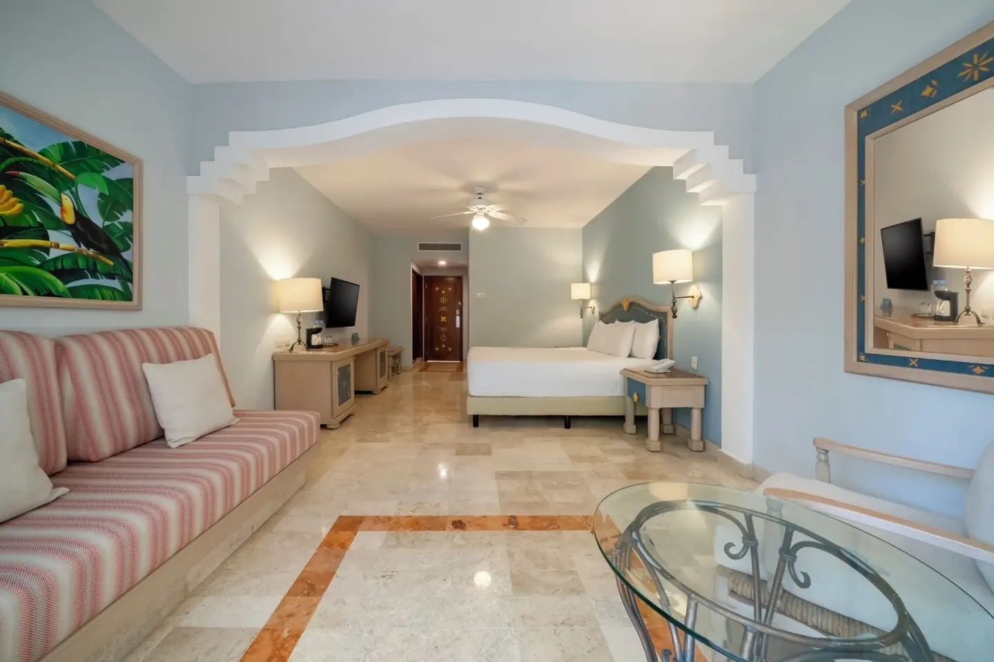 Junior Suite living area and bed at Iberostar Waves Paraíso del Mar with sofa, glass table, and TV.