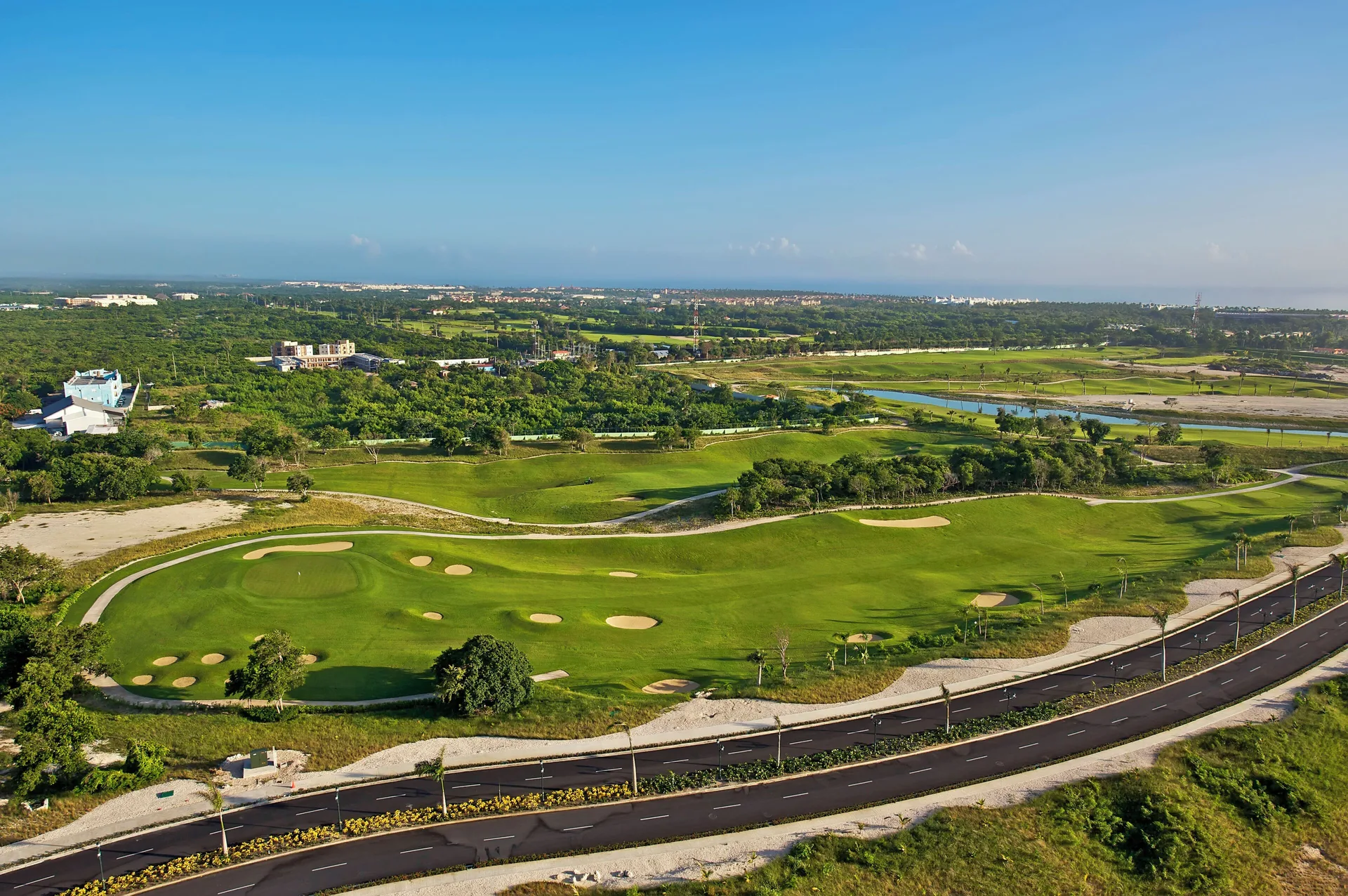 Aerial view of a golf course, roads, and greenery near Iberostar Waves Punta Cana.