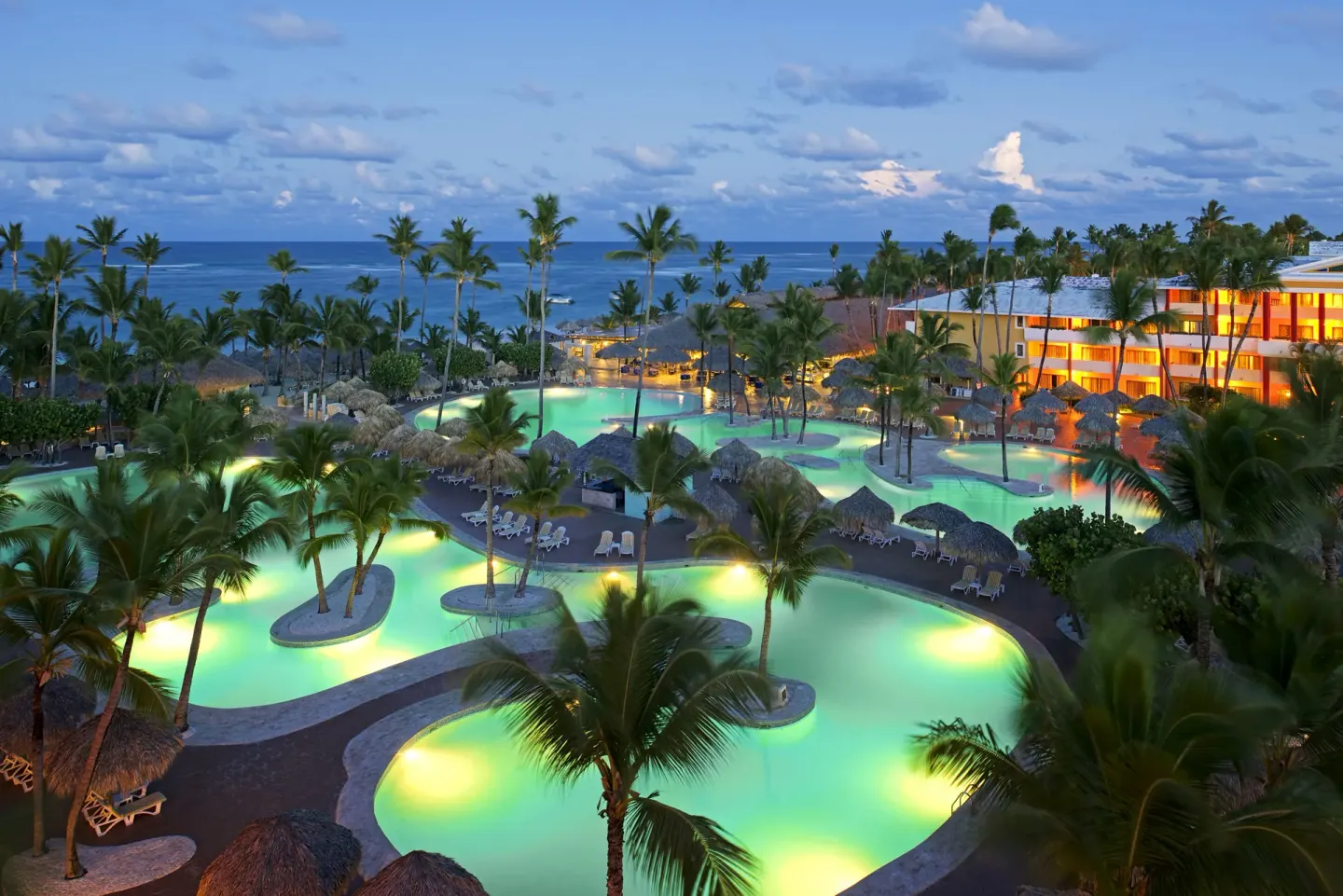 Evening aerial view of illuminated pools, palms, and ocean at Iberostar Waves Punta Cana.