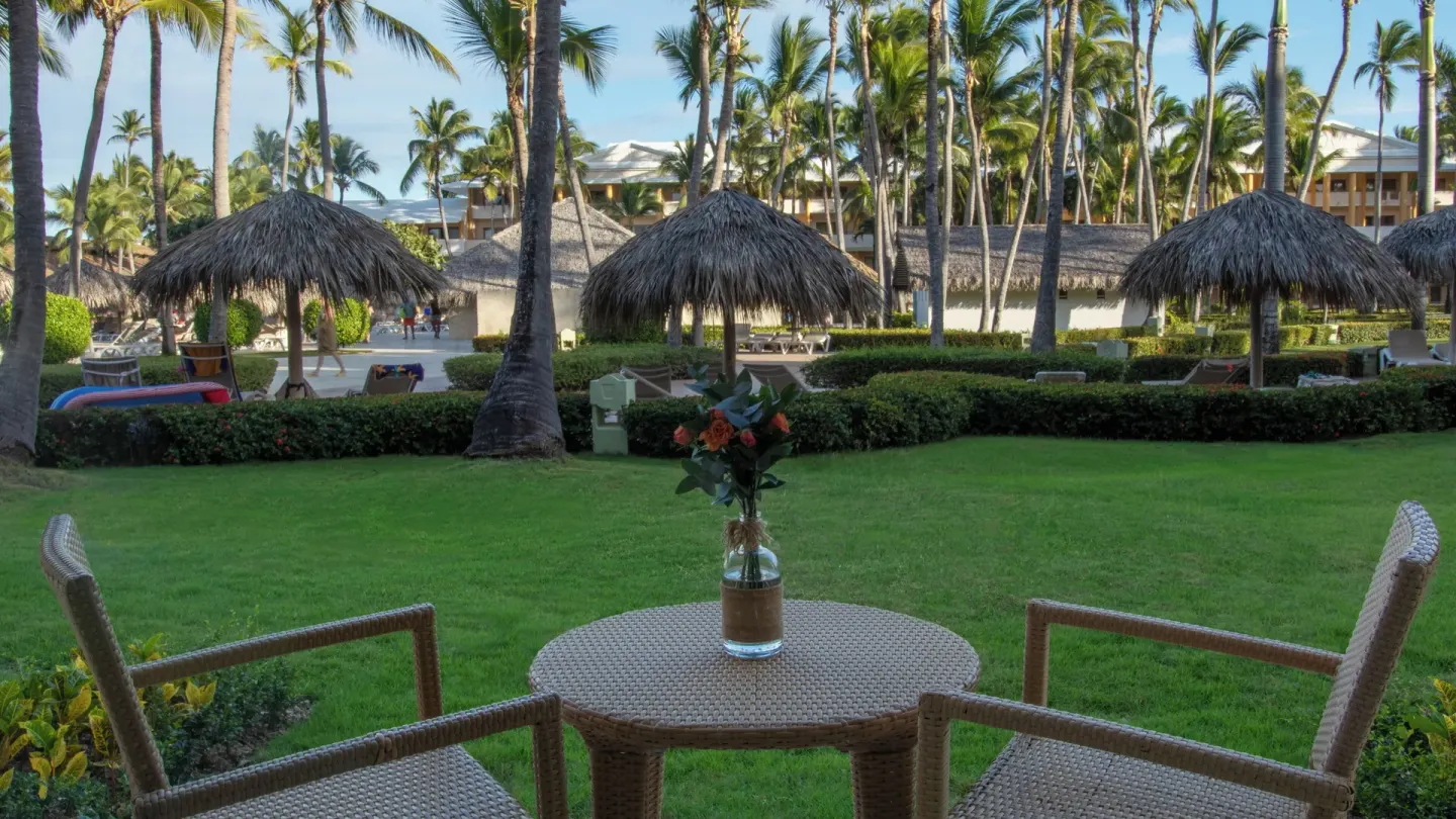 Patio table and chairs overlooking lawns, palms, and thatched shades at Iberostar Waves Punta Cana.