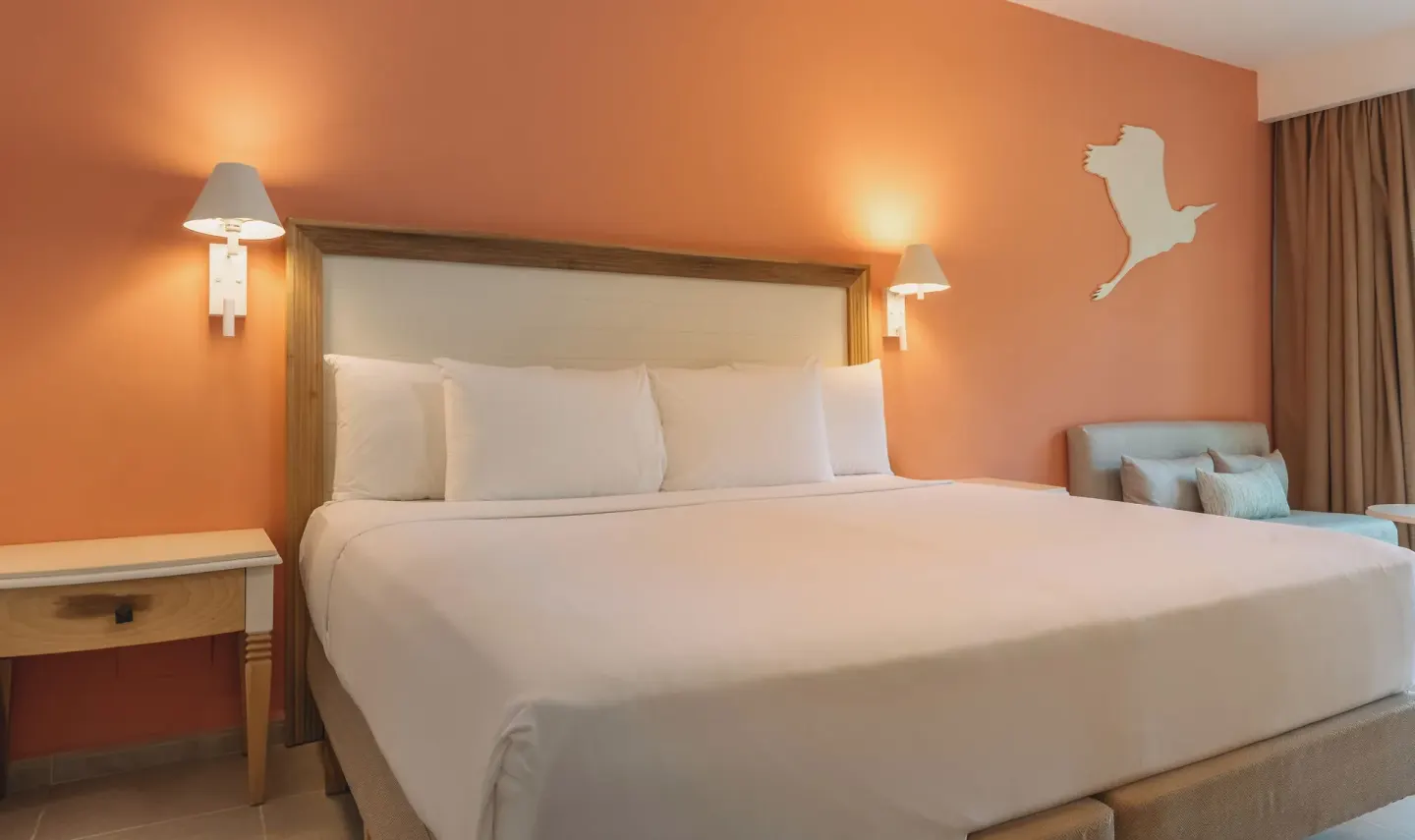 King bed with white linens against an orange wall at Iberostar Waves Punta Cana.