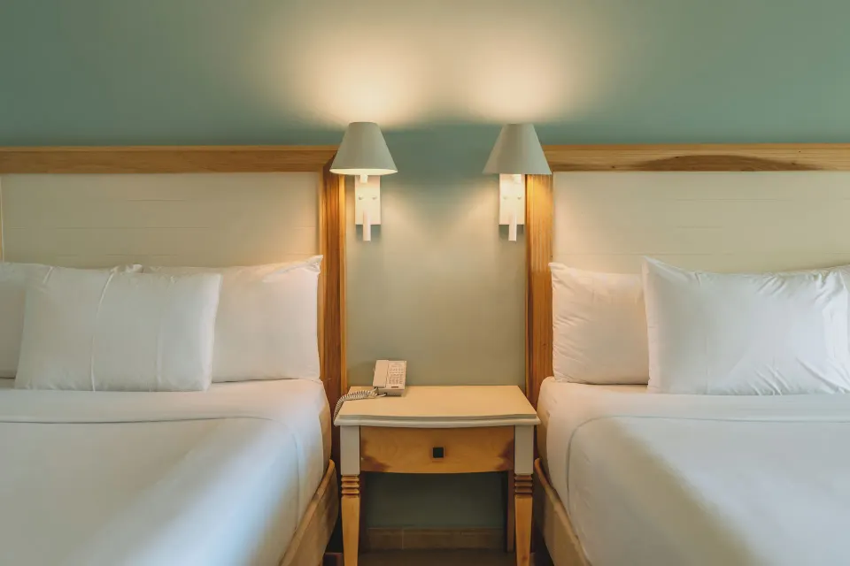 Two guest room beds with wall lamps and a shared nightstand at Iberostar Waves Punta Cana.