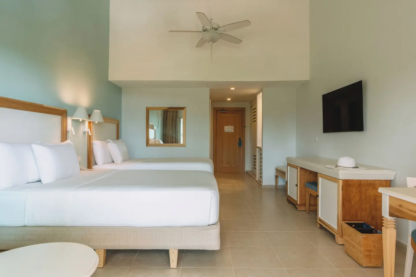 Two-bed guest room with TV, desk and ceiling fan at Iberostar Waves Punta Cana.