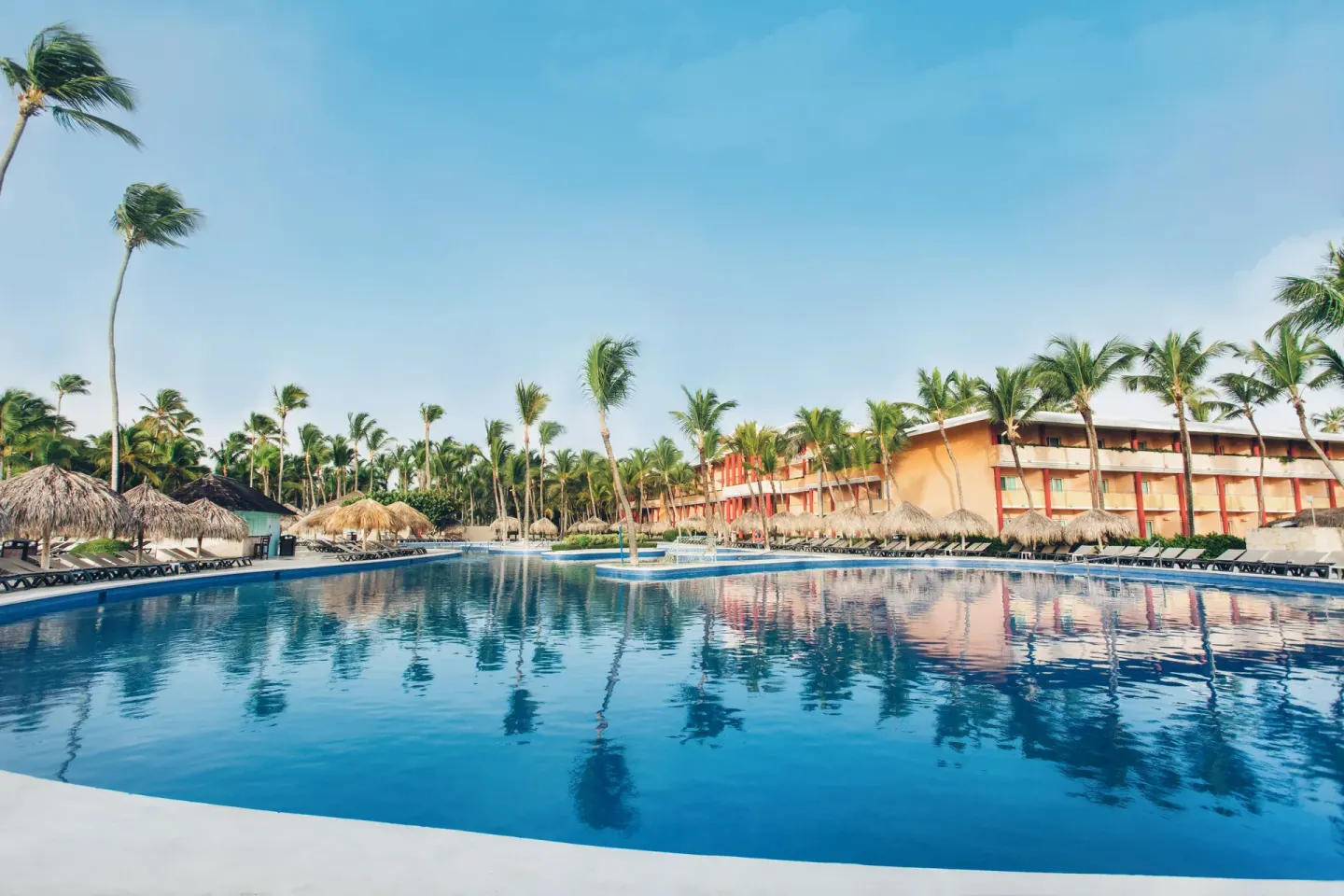 Large palm-lined pool with loungers and resort buildings at Iberostar Waves Punta Cana.