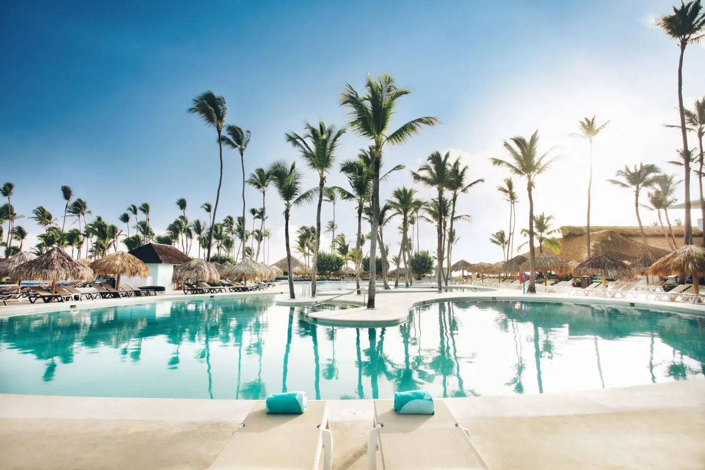 Sunny pool view with loungers, palms, and thatched umbrellas at Iberostar Waves Punta Cana.