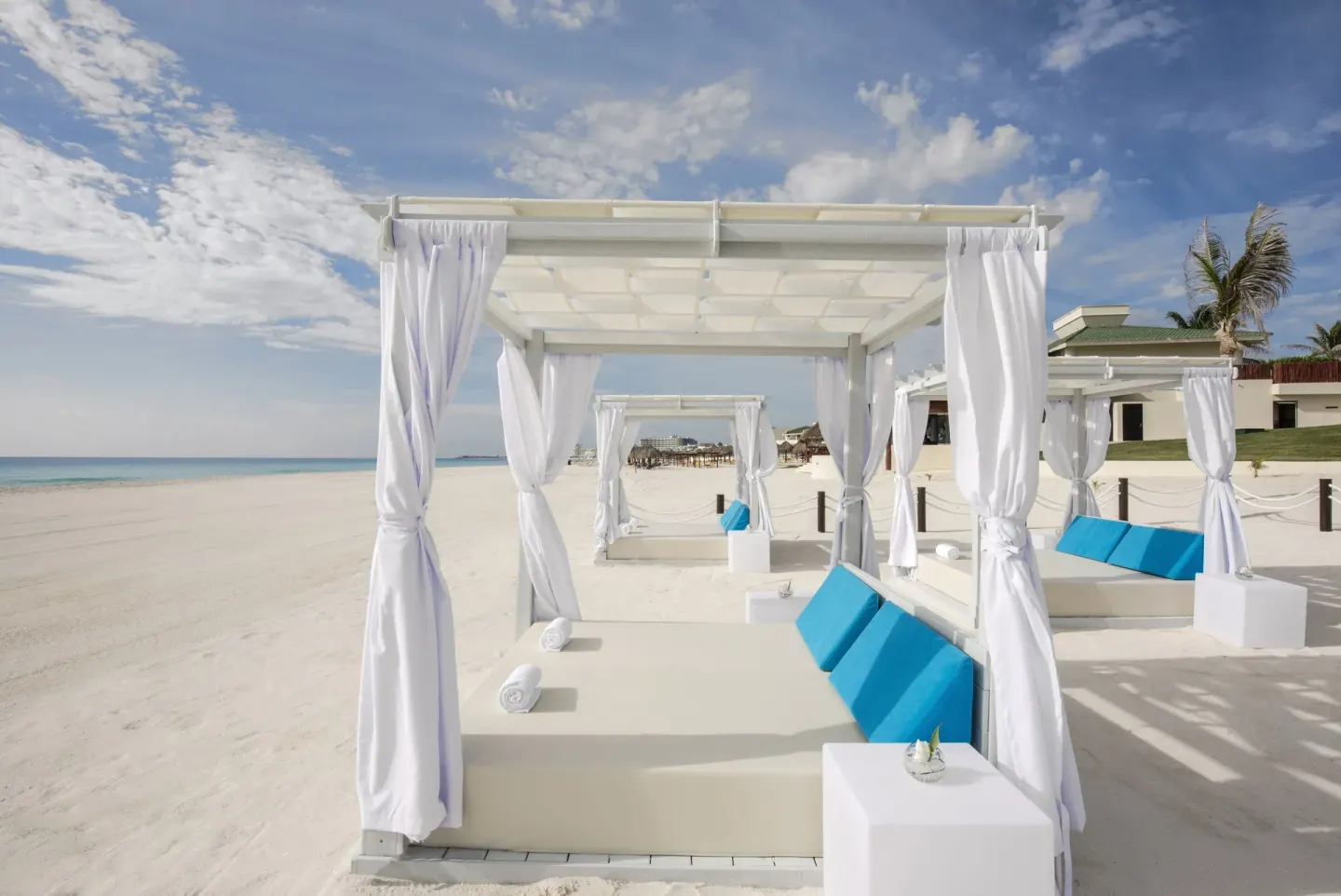 White beach cabanas with blue cushions on the sand at Iberostar Waves Punta Cana.
