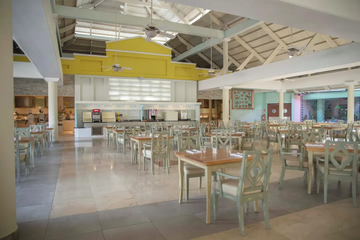 Buffet dining room with pale chairs, serving counters, and high ceilings at Iberostar Waves Punta Cana.