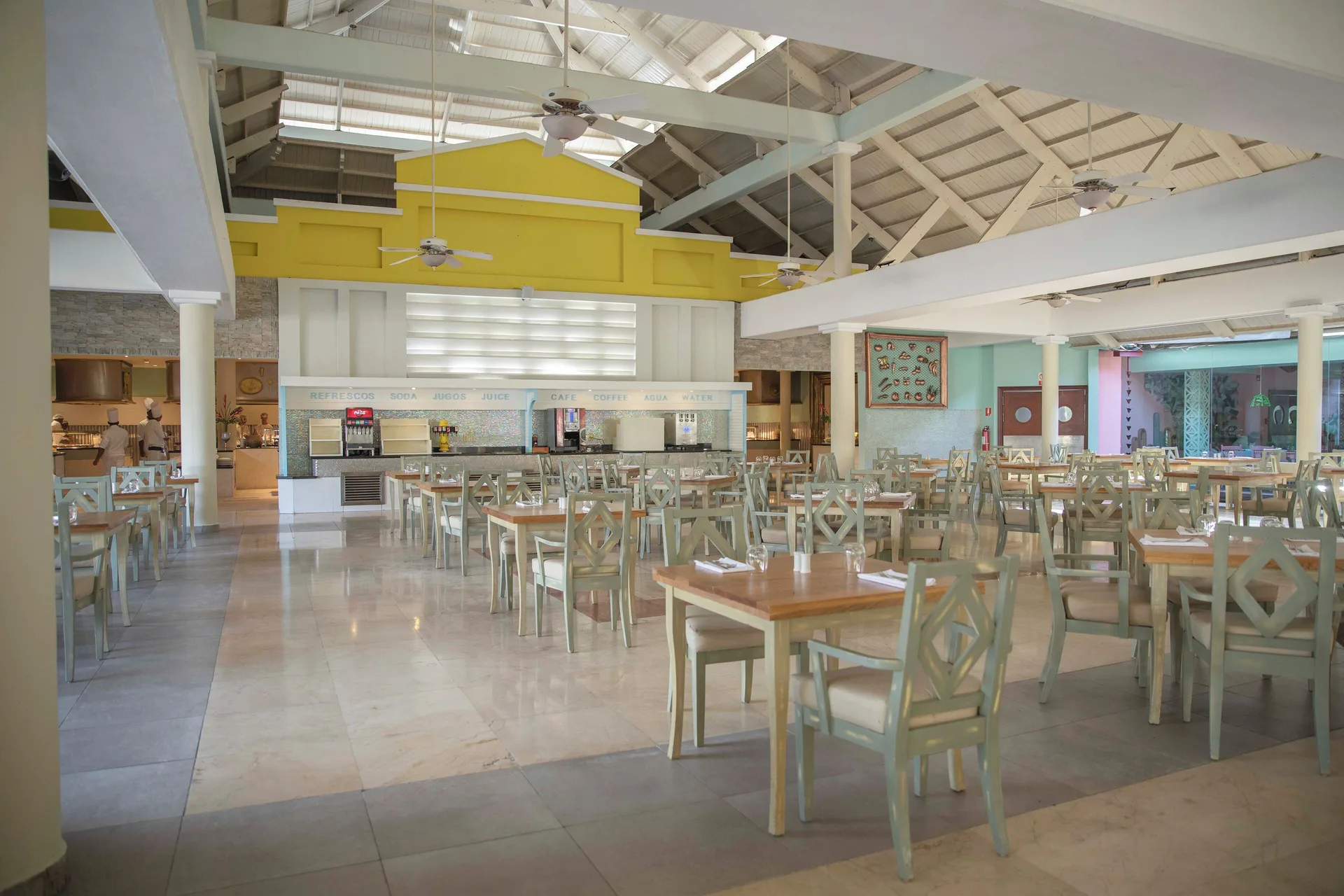 Buffet dining room with pale chairs, serving counters, and high ceilings at Iberostar Waves Punta Cana.