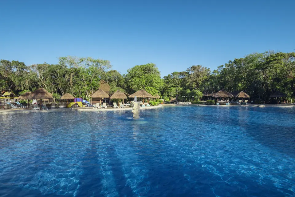 Expansive resort swimming pool with thatched cabanas and fountain at Iberostar Waves Tucán