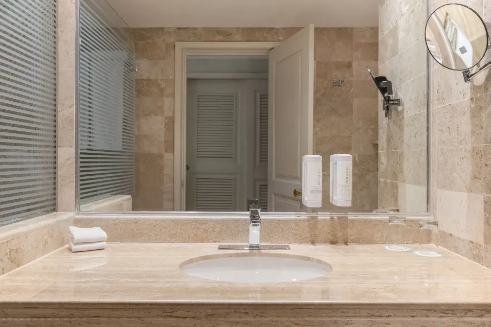 Marble sink and mirrored wall with soap dispensers in a guest bathroom at Iberostar Waves Tucán