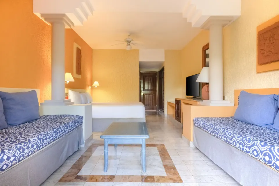 Warm-toned suite with king bed, twin daybeds and central table at Iberostar Waves Tucán