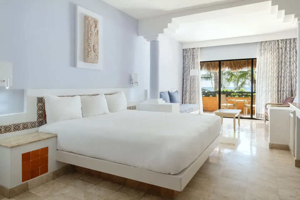 Bright junior suite with low-profile king bed and thatched-palapa balcony at Iberostar Waves Tucán