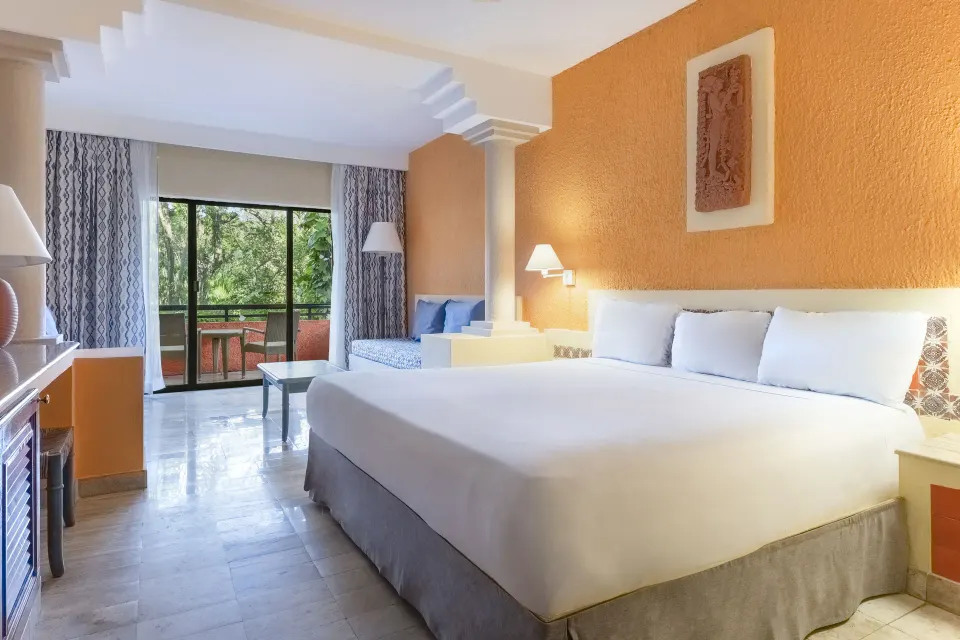 Large guest room with king bed and balcony framed by columns and orange accent walls at Iberostar Waves Tucán
