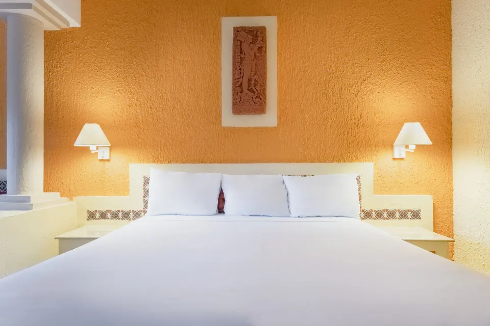 Close-up of king bed headboard against an orange textured wall at Iberostar Waves Tucán
